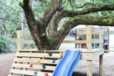 34 a platform built around a living tree, with a climbing wall and a blue slide is a cool space for kids’ playing and having fun