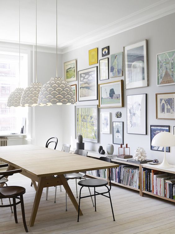 a Scandinavian dining room with a modenr table and black chairs, a free form colorful gallery wall and bookshelves