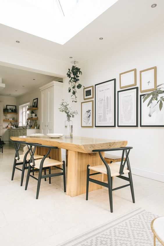 A Scandinavian dining space with a wood slab table, chic mid century modern chairs, an elegant monochromatic gallery wall