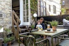 a Scandinavian patio with a wooden deck, grene metal furniture, potted plants and greenery and some pillows