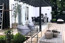 a Scandinavian terrace with a wooden deck, a woven coffee table, black metal chairs, a corner bench and greenery around