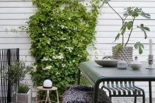a Scandinavian terrace with dark green metal furniture, climbing greenery and blooms, potted plants and a rattan chair