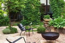 a beautiful modern backyard with a black metal fire bowl and black metal chairs plus lots of greenery around