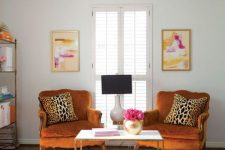 a bright and chic space with rust-colored vintage chairs, a pink printed rug, a storage unit and bold artworks