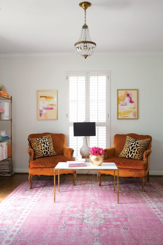 A bright and chic space with rust colored vintage chairs, a pink printed rug, a storage unit and bold artworks