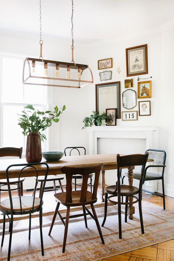 a charming vintage dining room with a vintage table and mismatching chairs, a faux fireplace and a mini gallery wall over it