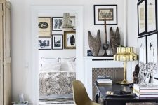 a chic and refined home office with a black vintage desk, a gold chair and a gold table lamp, a largre gallery wall and a chandelier
