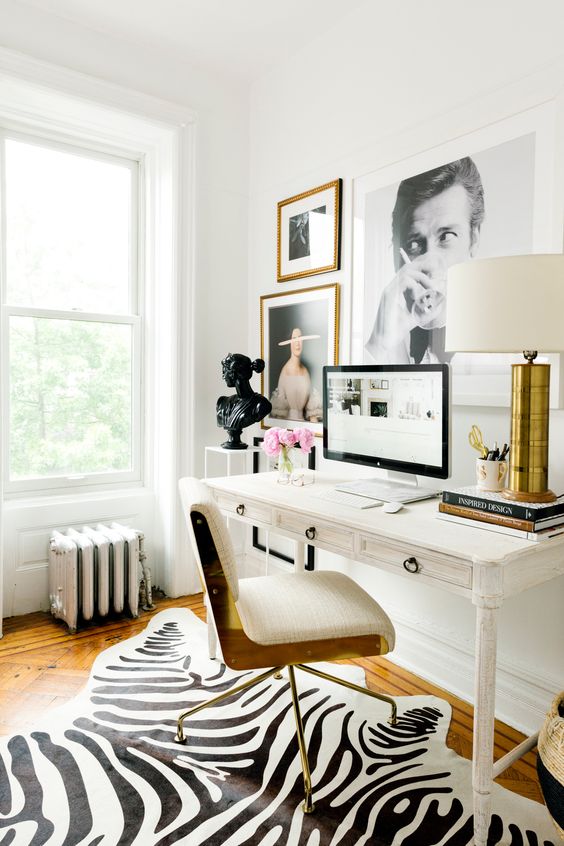 a chic glam home office in creamy shades, with a vintage desk, a creamy and gold chairs, a statement gallery wall and a table lamp