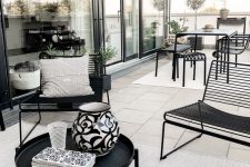 a chic modern terrace done in neutrals and accented with black metal furniture – a table and chairs, loveseats and a round table