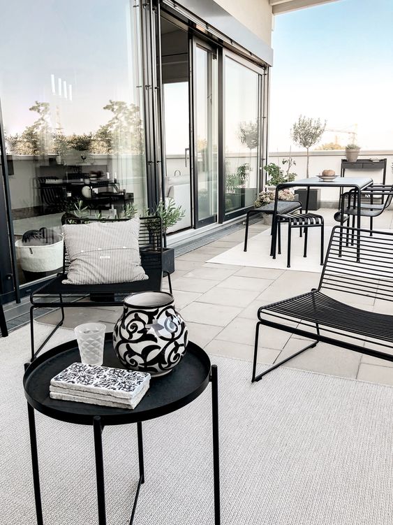 A chic modern terrace done in neutrals and accented with black metal furniture   a table and chairs, loveseats and a round table