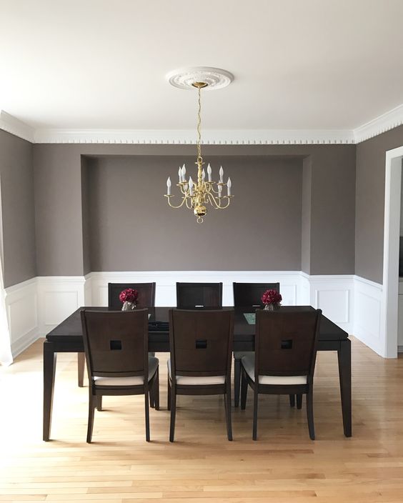A clean mid century modern to vintage dining room with creamy paneling, a black table and dark chairs, a gold chandelier
