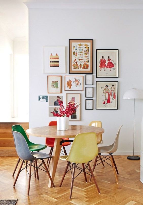 a cool and bright dining room with a stained table and colorful chairs, a bold gallery wall and bright blooms