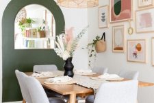 a mid-century dining room with a stained table and grey chairs, a green accent wall, a pastel gallery wall