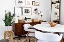 a mid-century modern dining room with a white table and neutral chairs, a stained credenza, a free form gallery wall and a mirror