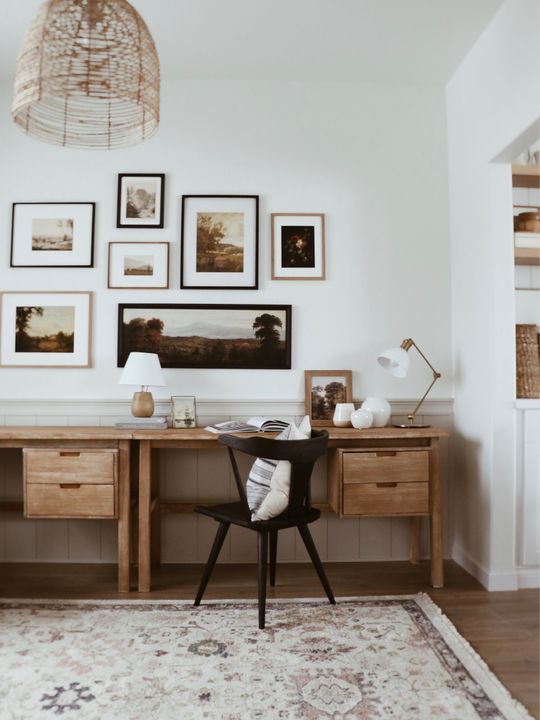 A mid century modern home office with a shared stained desk, a black chair, a moody gallery wall and a woven pendant lamp
