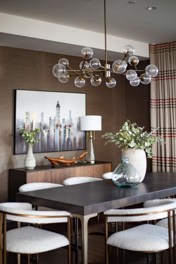 A mid century modern taupe dining room with a credenza, a dark table and creamy chairs, a lovely chandelier