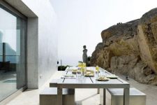 a minimalist terrace next to the rock, with a metal dining table and concrete stools plus a sea view is a cool space