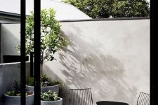 a minimalist terrace with a tall fence, a black metal dining set, potted plants in large pots and a mosaic tile floor