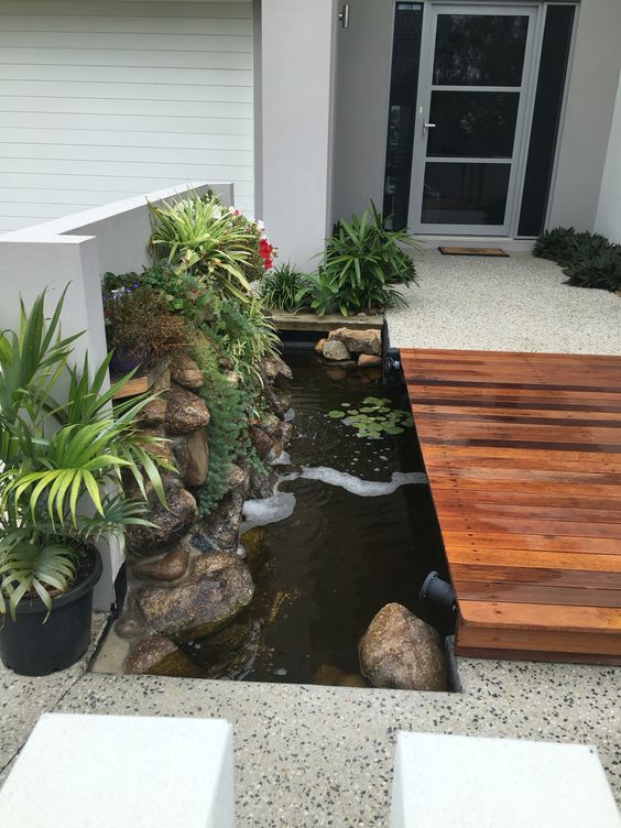 a modern entrance with a stained path, a water feature with rocks and greenery plus spotlights is great and chic