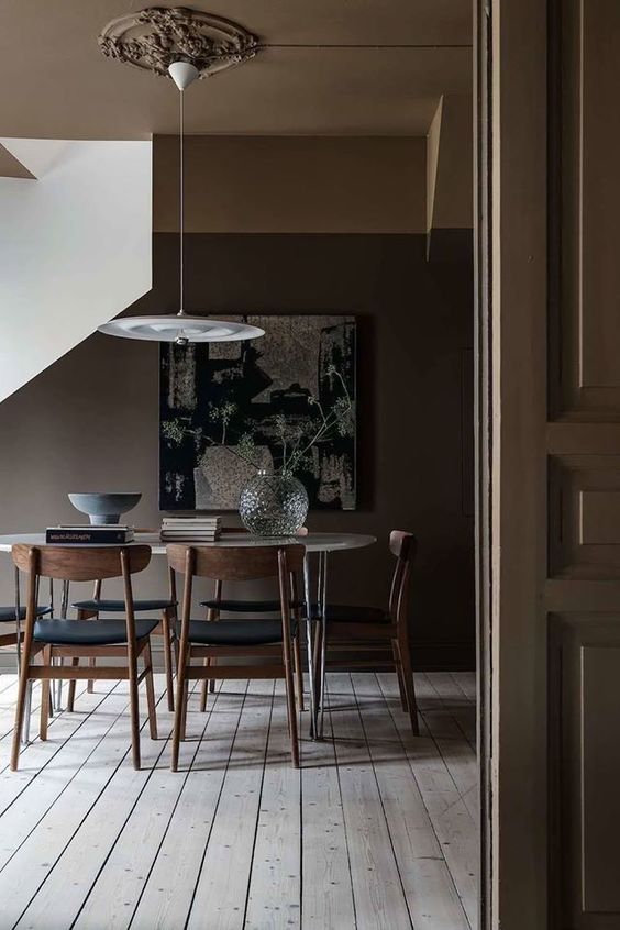 a moody all-taupe dining space with a neutral floor, an oval hairpin leg table, black chairs and a pendant lamp