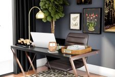 a moody home office with black walls, a brown desk and a chair, a geo printed rug, a lovely gallery wall and a potted tree