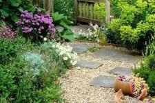 a pretty countryside garden with greenery and blooms, with planters, a gravel pathway and some stone steps