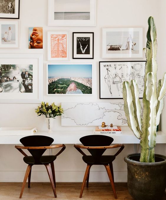 a pretty mid-century modern home office with a wall-mounted shared desk, black chairs, a bright gallery wall and a potted cactus