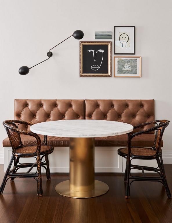 a refined dining space with a banquette seating, a round table, rattan chairs, a mini gallery wall and a black sconce