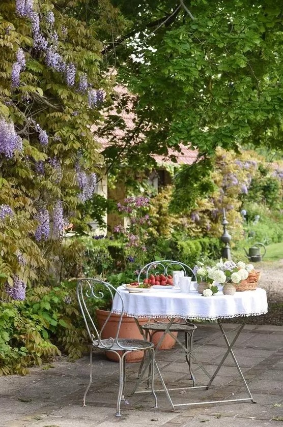 A small and lovely Provencal outdoor space with a metal table and chairs and some blooms and greenery around   who needs more than that