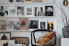 a stylish gallery wall with multiple white ledges, various magazines, books and artworks plus a lamp that accents it