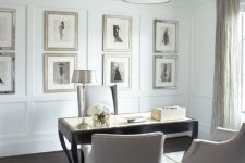 a very elegant and refined neutral home office with paneling and a vintage gallery wlal, a black vintage desk, neutral chairs and a chandelier on chain