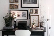 an eclectic home office with a black vintage desk, a white chair, a monochromatic gallery wall and potted greenery and candles