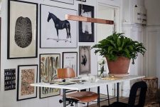 an eclectic home office with a lightweight desk, a plywood and black soft chair, an oversized gallery wall with potted plants