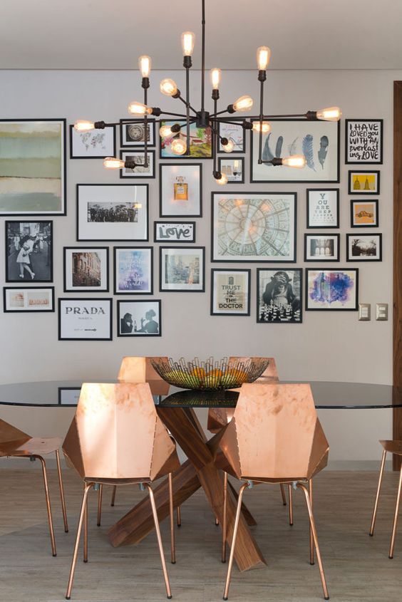 an elegant dining room with a glass table, copper faceted chairs, a chic chandelier and a free form gallery wall