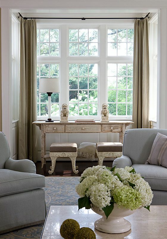 a bay window in a niche is done with railing all along the window and mustard curtains that can cover each part of it