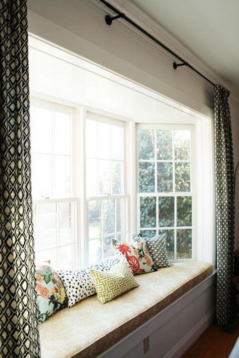 a bow window with a stylish windowsill daybed and pillows and printed curtains over the whole window to make the ceiling look higher