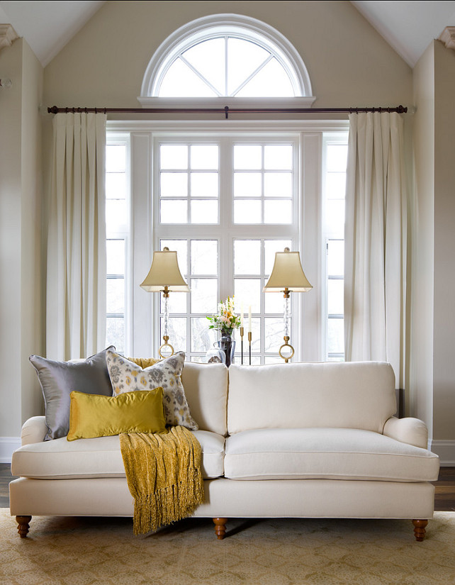 A large window with a half circle piece done with creamy drapes and the piece above stays uncovered   a stylish and cool solution