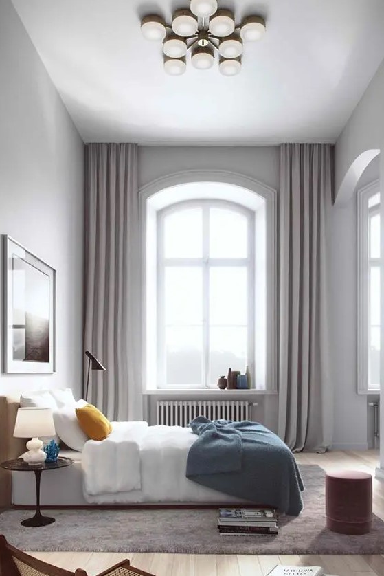 A modern bedroom with a double height ceiling, an arched window done with grey curtains hanging under the ceiling to accent this height