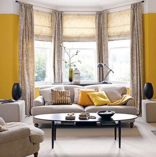 a bright grey and yellow living room with a bow window done with printed curtains, grey seating furniture and a refined table
