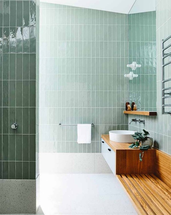 A bathroom clad with mint skinny stacked tiles, white terrazzo tiles on the floor, a floating vanity with a built in bench