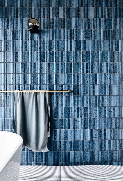a chic contemporary bathroom with a grey floor, a blue and navy skinny tile wall and brass touches looks chic