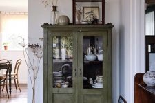 a green shabby chic cabinet with glass doors is used for storing tableware and porcelain in a rustic dining room or kitchen