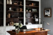 a home office with built-in shelves, a stained desk, a pendant lamp and a black and white artwork plus brass touches
