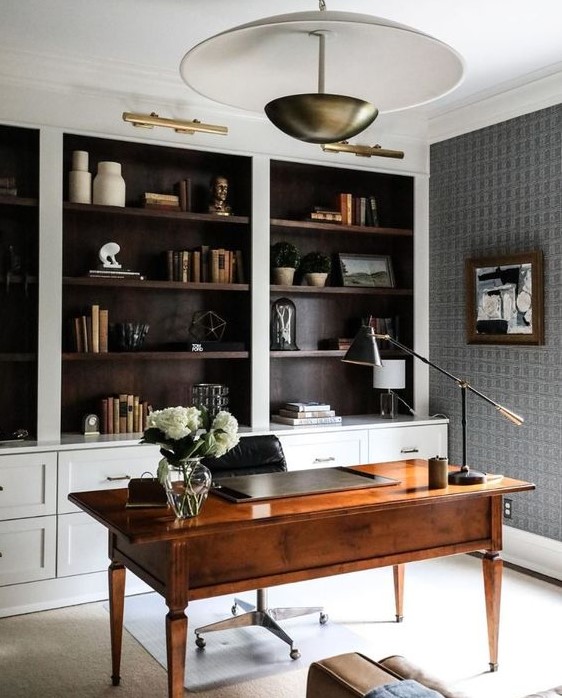 a home office with built-in shelves, a stained desk, a pendant lamp and a black and white artwork plus brass touches