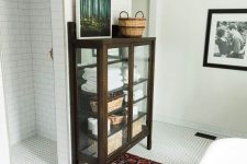 a modern bathroom with a bright rug, white tiles all over and a vintage dark stained glass armoire