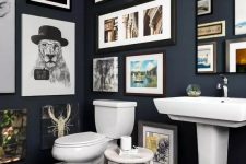 a navy bathroom with a gallery wall that takes all the blank wall space, white appliances and a mirror integrated into this art spot