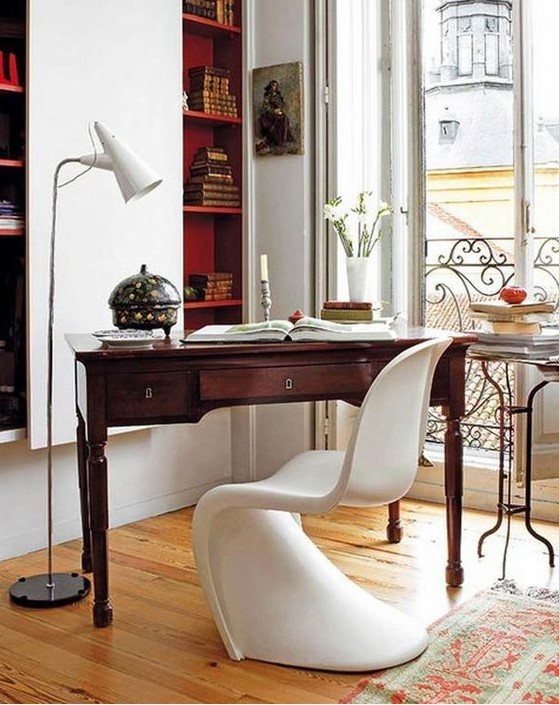 A refined contemporary home office with built in bookshelves, a vintage stained desk, a white sculptural chair and a small table
