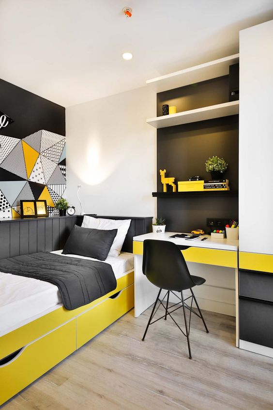 A small and brigth teen room with a built in desk and shelves, a bold yellow bed with black and white bedding and bold art on the wall
