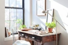 a small and cozy workspace with a dark stained desk, a metal chair, potted plants and pretty artworks plus a floor lamp