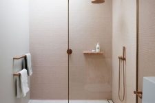 a small minimalist bathroom with pink walls, a printed tile floor, a glass divider and touches of rose gold